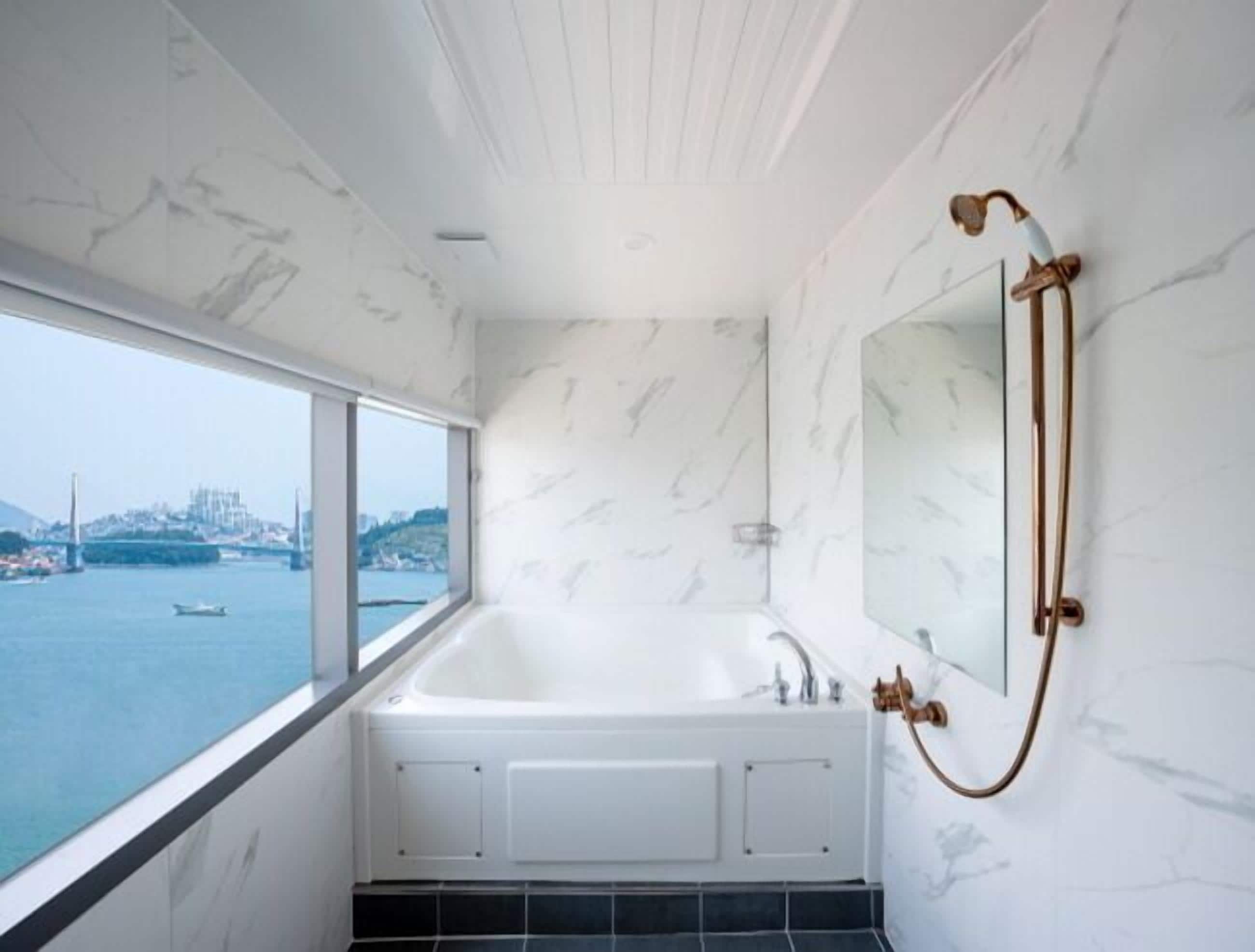 A modern bathroom with a large bathtub, a view of a body of water, and a cityscape in the background.