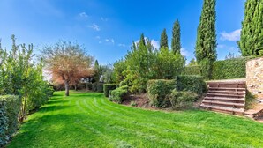 Un jardín bien cuidado con diversos árboles, un césped impecable y un muro de piedra con escalones.