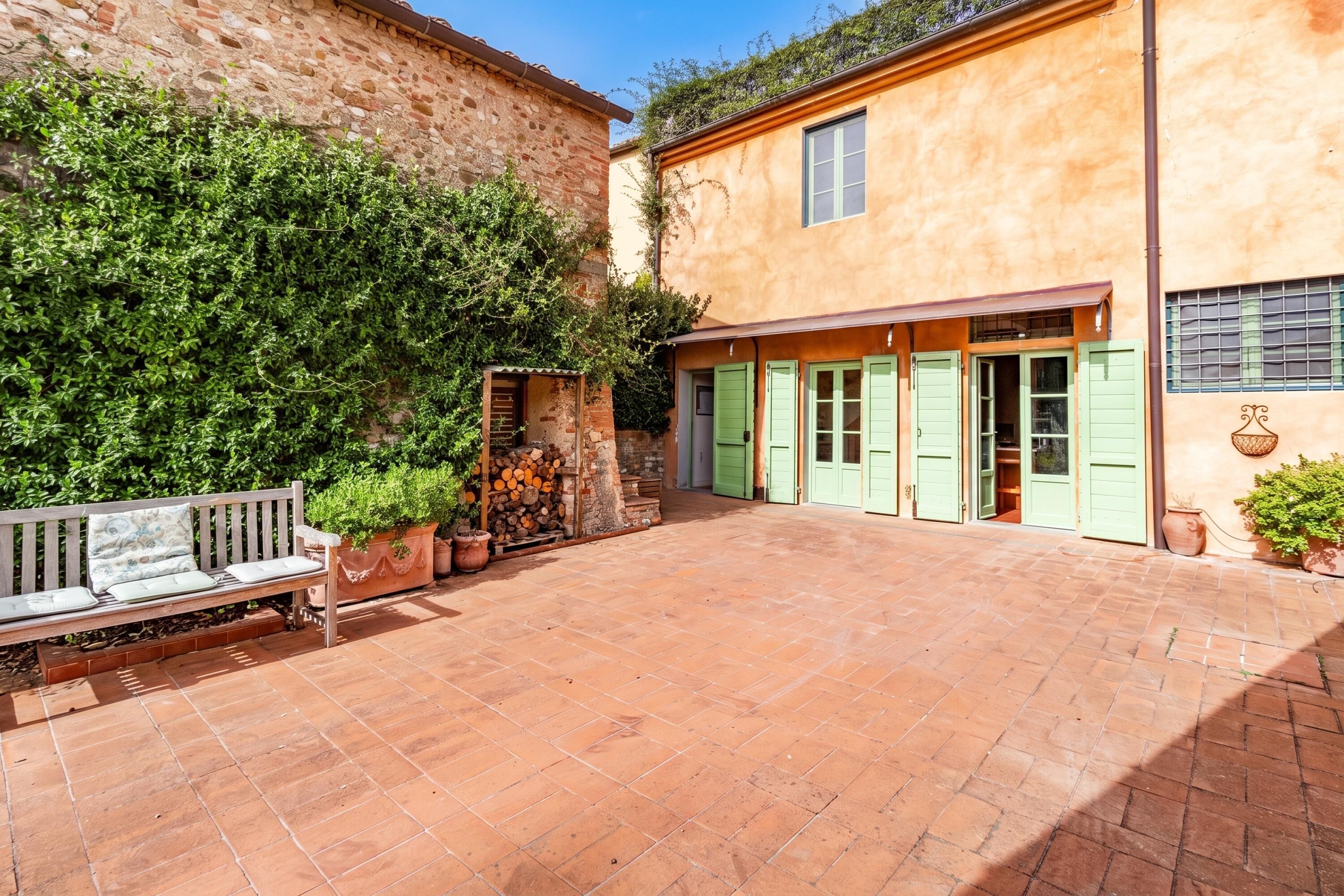 A courtyard with a bench, a wooden fence, and a building with green shutters.