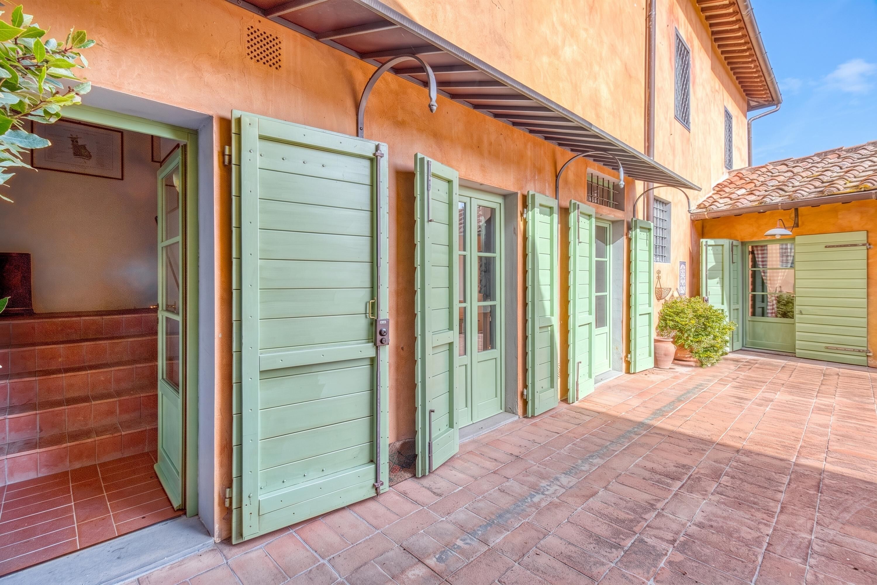 Un bâtiment avec plusieurs portes vertes, une cour dallée et un pot de fleurs.