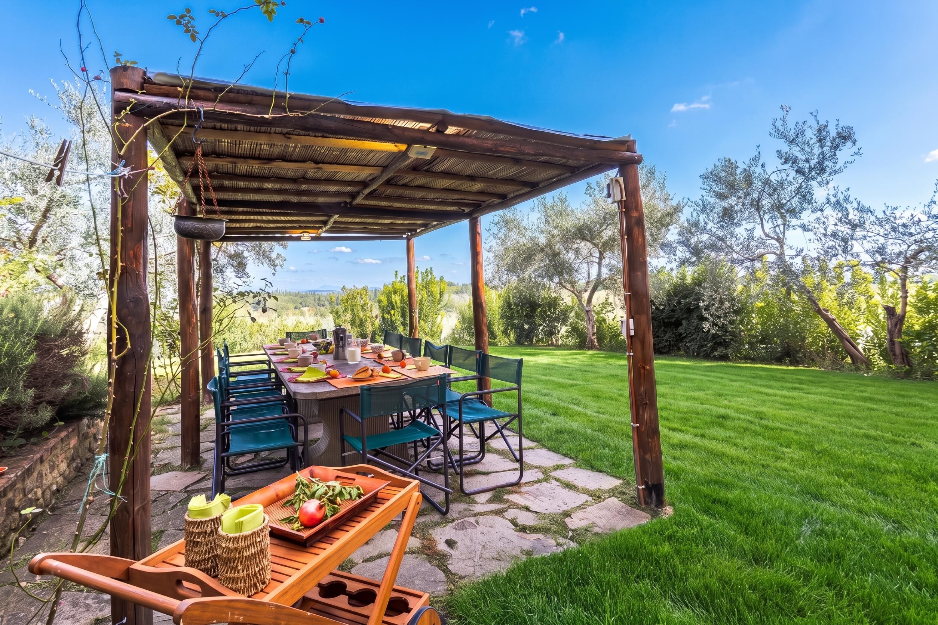 Un área de comedor al aire libre con pérgola, suelo de piedra y vistas a un césped cuidado y árboles.