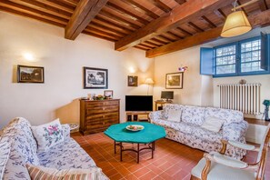 A living room with a wooden ceiling, a television, a sofa, a table with a plate of food, and a window with blue shutters. - Villa Salivolpe Amazing Chianti View 8, San Casciano VDP, Italy (San Casciano VDP)