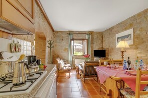 A cozy kitchen with a gas stove, wooden chairs, a dining table with a pink tablecloth, and a stone wall. - Apt Ciclamino Shared Pool & Activities in Tuscany, Montaione, Italy (Montaione)