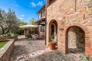 A courtyard with a brick building, a covered patio area, and potted plants. - Apartment Ciclamino Shared Pool & Activities in Tuscany, Montaione, Italy (Montaione)