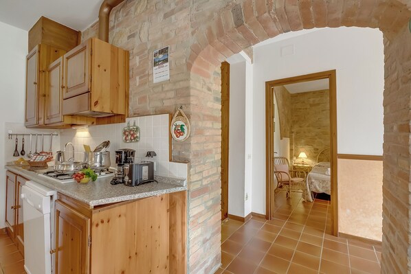 A kitchen with wooden cabinets, a built-in stove, and a brick wall. - Apt Ciclamino Shared Pool & Activities in Tuscany, Montaione, Italy (Montaione)