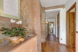 A hallway with a brick wall, a potted plant with white flowers, and a tiled floor. - Apt Ciclamino Shared Pool & Activities in Tuscany, Montaione, Italy (Montaione)