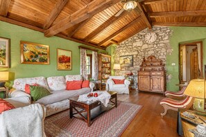 A cozy living room with a wooden ceiling, a stone wall, and a fireplace. There is a sofa, a coffee table, and a lamp. - Traditional Karst House Rozina /w Garden, Dutovlje, Slovenia (Dutovlje)