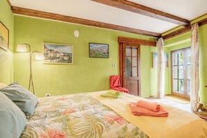 Un dormitori amb un llit, una cadira, una finestra i dos quadres penjats a la paret.