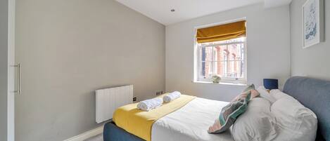 A bedroom with a bed, a window with a view, a radiator, and a blue bench.