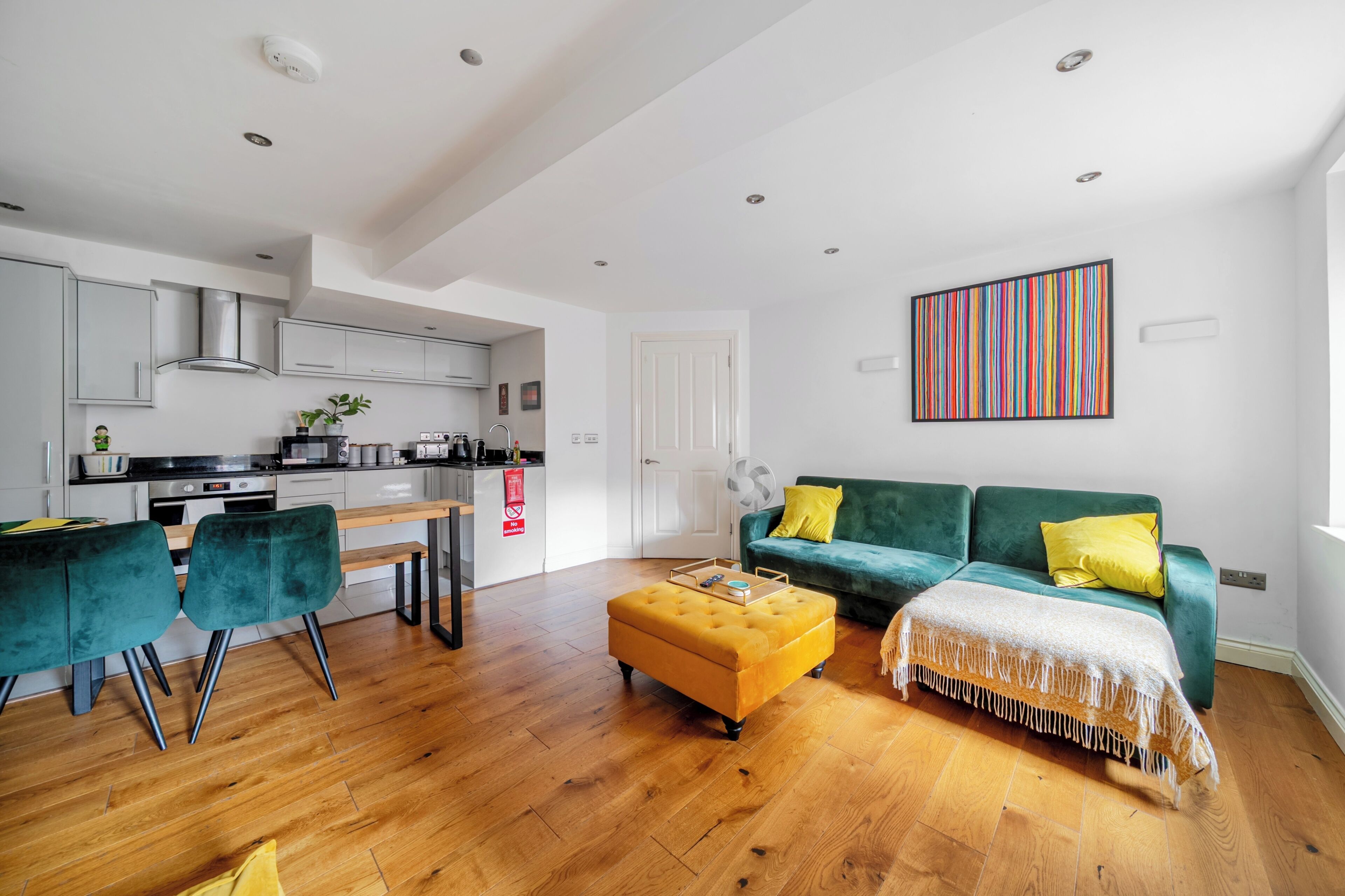 Ein modernes Wohnzimmer mit einer Küche, einem grünen Sofa und einem Holzesstisch.
