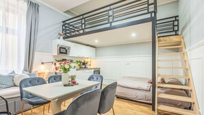 Ett kompakt bostadsutrymme med en våningssäng, en matplats med stolar, ett kök och en trappa.