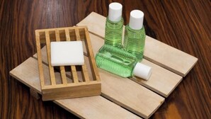 Una bandeja de madera con una barra de jabón blanco y dos botellas verdes sobre una superficie de madera.