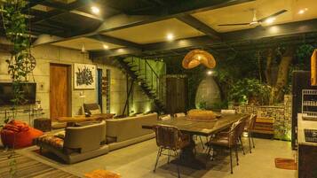 A modern living room with a sofa, dining table, and chairs, a staircase, and a large hanging light fixture.