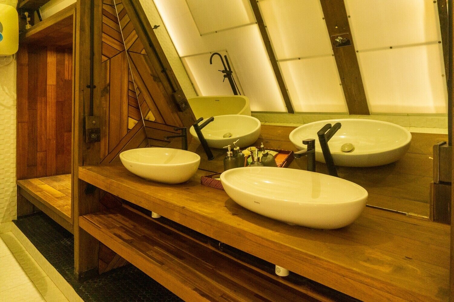 A bathroom with three sinks, wooden benches, and a mirror.