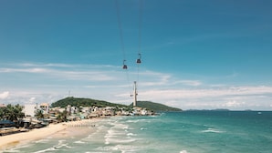 Un pueblo costero con playa, un teleférico y una colina con edificios.
