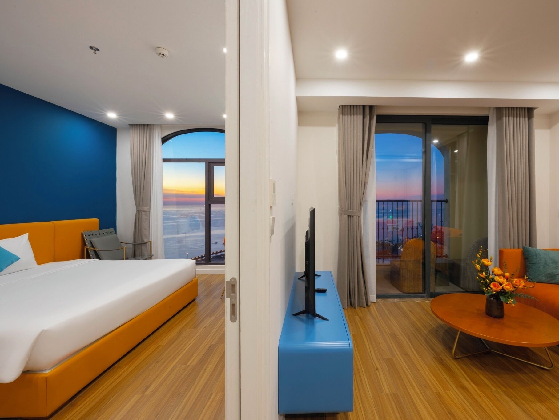 Une chambre d’hôtel avec un lit, une télévision, un bureau, une chaise, un balcon avec vue et une table décorée de fleurs.