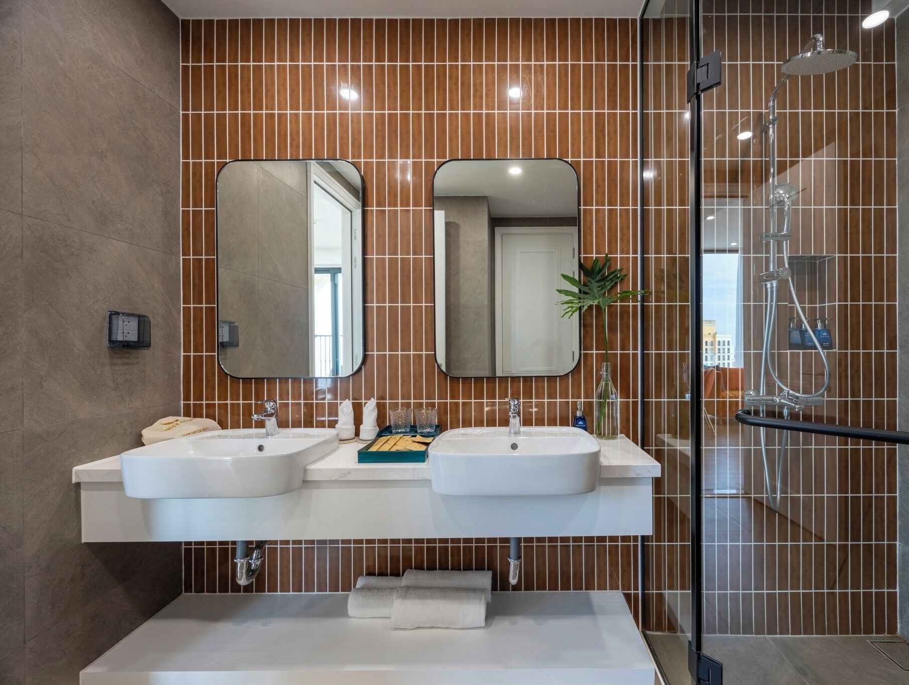 A modern bathroom with two sinks, a glass shower enclosure, and a large mirror above the sinks.