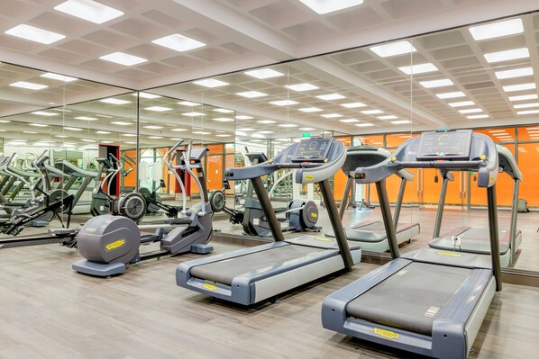 Un gimnasio con cintas de correr, elípticas y otros equipos de cardio, con un espejo grande y detalles en naranja.