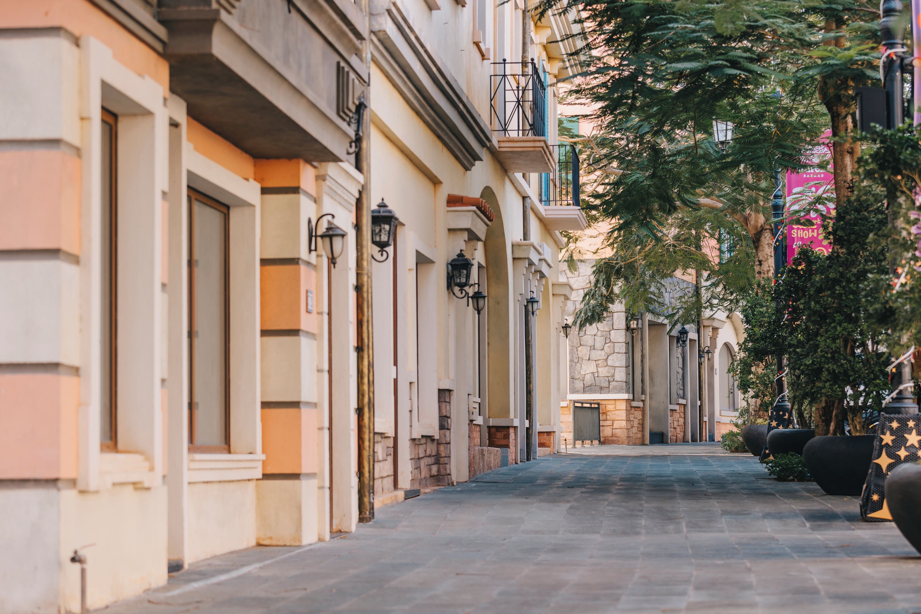 A narrow street lined with buildings, featuring balconies, stone facades, and outdoor lighting fixtures.