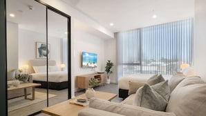 A modern hotel room with a large bed, a sofa, a coffee table, a TV, and a balcony with a view. - Modern Studio With Rooftop and BBQ Access (Perth)