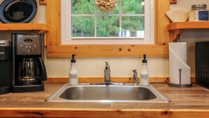 Una cocina con cafetera, jabón de manos y detergente para platos sobre la encimera, una ventana con vistas a zonas verdes y armarios de madera.