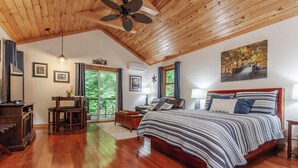 A spacious bedroom with a large bed, wooden flooring, a ceiling fan, and a view of the outdoors through a sliding glass door. - Starry Night- Honeymoon Cabin| Hot Tub| Near GSMNP (Bryson City)