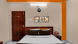 A hotel room with a bed, a wooden door, a nightstand with a vase of flowers, and three framed pictures on the wall. - Classic Sri Sai Guru Comfort (Bengaluru)