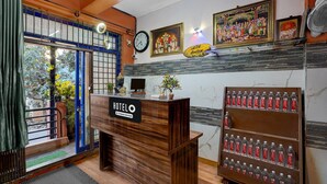 A hotel reception desk with a sign reading "HOTEL & Company Service." There are framed pictures on the wall, a clock, and a water dispenser. - Classic Sri Sai Guru Comfort (Bengaluru)