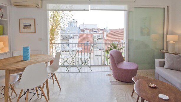 Un salon moderne comprenant un coin repas, un balcon avec vue sur les immeubles et un canapé.