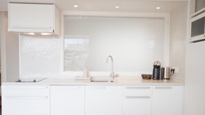 Une cuisine moderne avec des meubles blancs, un évier en acier inoxydable et une fenêtre donnant sur des immeubles.