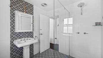 A bathroom with a patterned floor, a pedestal sink, a glass shower enclosure, and a white door.