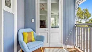Una silla azul con cojines amarillos frente a una puerta blanca, una terraza de madera y una barandilla blanca.