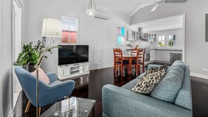 Una sala de estar moderna con una televisión de pantalla plana, un sillón azul, un sofá y un comedor con mesa y sillas.