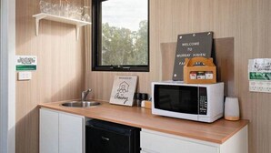 Eine moderne Küche mit Holztischplatte, einer Mikrowelle, einem Spülbecken und einem Fenster mit Blick auf Bäume.