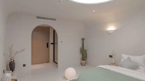 A modern bedroom with a bed, a round light fixture, a cactus, and a door leading to another room. - Lugu Lake September Sky Stay (Ninglang)