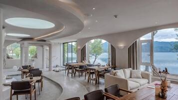 A spacious interior with a dining area, seating arrangements, and large windows offering a view of a lake.