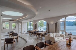 Un interior espacioso con comedor, asientos y grandes ventanas que dan a un lago.