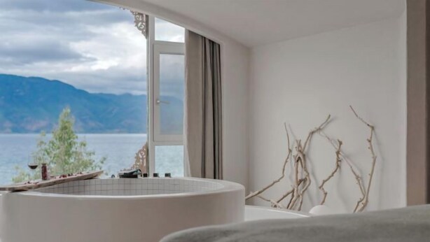 A modern bathroom with a bathtub, a window with a view of mountains, and a decorative branch on the wall. - Lugu Lake September Sky Stay (Ninglang)