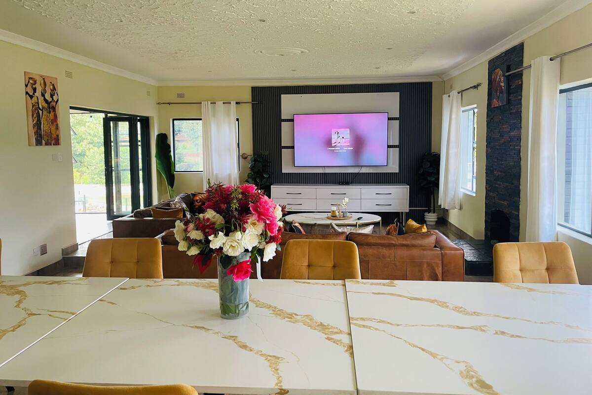 A modern living room with a large TV, comfortable seating, and a dining area with a marble table.