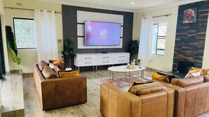 A modern living room with a large flat-screen TV, leather sofas, a coffee table, and a fireplace.