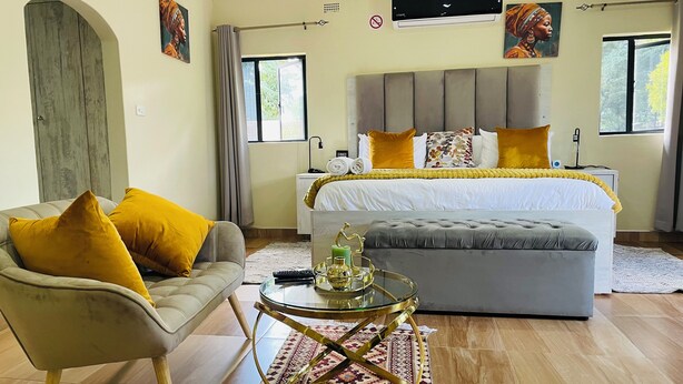 A bedroom with a large bed, a sofa, a glass coffee table, and artwork on the walls.