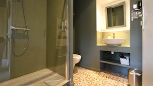 A bathroom with a glass shower enclosure, a toilet, a sink with a mirror above it, and a patterned floor. - Chambre Tilleul 1 st floor (ST MALO)