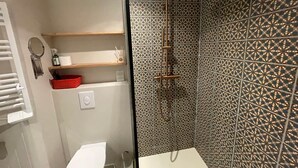 Et badeværelse med bruser, toilet, vask og hylder med toiletartikler.