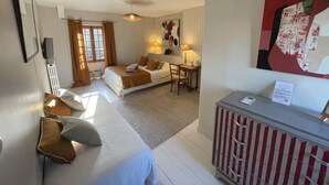 Et hotelværelse med seng, skrivebord, stol, radiator, et vindue med gardiner og et billede på væggen.