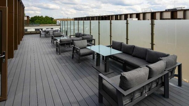 Eine Terrasse mit Gartenmöbeln, darunter Sofas und Tische, sowie eine Glasabtrennung.