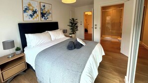 Ein modernes Schlafzimmer mit Bett, Nachttisch, Lampe und abstrakter Wandkunst.