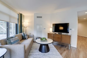 A modern living room with a sofa, a round coffee table, a television, and a cabinet. - Sojourn | VA Square | 2 BR (Arlington)