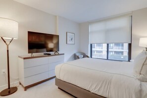 Ein Hotelzimmer mit einem Bett, einem Fernseher auf einem Schrank, einem Schreibtisch mit Stuhl und einem Fenster mit Jalousien.