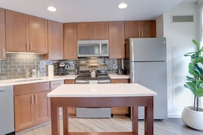 A modern kitchen with wooden cabinets, stainless steel appliances, and a central island. - Sojourn | VA Square | 2 BR (Arlington)