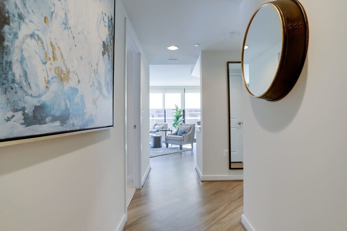 A hallway with a large abstract painting, a round mirror, and a view into a living area with a balcony.